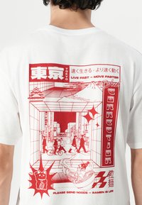 Witte T-shirt met een rood grafisch ontwerp van een straatbeeld in Tokio, met gestileerde figuren, de Mount Fuji en een illustratie van een ramenkom.