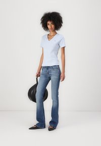 Tricou bleumarin deschis cu guler în V, design ajustat, asociat cu blugi evazați de culoare albastră, decolorat. Pantofi negri cu vârf ascuțit și o geantă rotundă neagră completează aspectul.