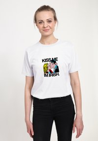 Bílé tričko s grafikou páru, který se líbá, a nápisem „KISS ME I'M IRISH“ v tučných černých písmech. Krátké rukávy, standardní střih.