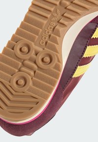 Adidas sko sål med et tekstureret mønster, fremstillet af et tan gummimateriale, lilla overdel, lyserøde accenter og genkendelige logoer.