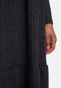 Robe texturée gris foncé avec des rayures verticales, manches longues et un ourlet superposé. Une main est visible au bord du tissu.