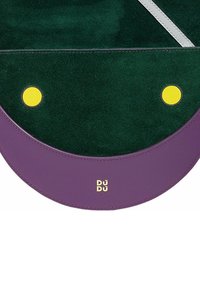 Borsa rotonda realizzata in suede verde con una base in pelle viola, un accento circolare giallo e un logo dorato "DÜDÜ".