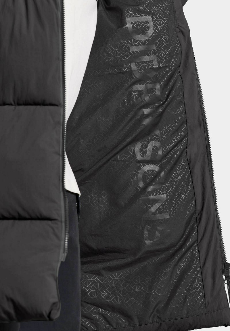 Schwarze Steppjacke mit einem Reißverschluss; das Innere hat eine matte Textur mit einem geometrischen Muster und Schriftzügen.