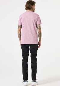Roze gemêleerd t-shirt met korte mouwen, gecombineerd met zwarte slim-fit broeken en witte sneakers met groene accenten. Tatoeages zichtbaar op de armen.