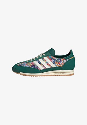 Baskets Adidas vertes et blanches avec des panneaux en tissu floral et des lacets blancs, montrées de profil sur fond blanc.