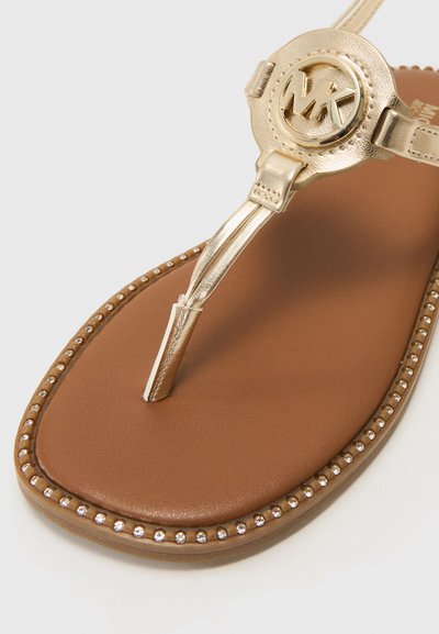 Sandália tipo thong em tom dourado com logo MK, palmilha acolchoada castanha e detalhes decorativos em pérolas ao longo da borda. Material sintético suave.