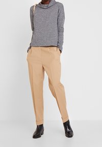 Grå strukturerad tröja med krage, kombinerad med beige plisserade byxor. Svarta stövletter fulländar outfiten. Slät tyg och avslappnad passform.