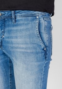 Vaqueros de mezclilla azul deslavados con un ajuste slim. Incluye bolsillos frontales, costuras sutiles y detalles de hardware metálico.