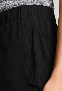 Schwarze Sportshorts mit einem strukturierten Bund und seitlichen Taschen. Mit einem kleinen schwarzen Logo auf der unteren linken Seite. Glattes Material.