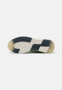 Suola di una sneaker con sezioni in gomma bianca e blu scuro, battistrada a forma di X e materiale traslucido nelle aree del tallone e della punta.