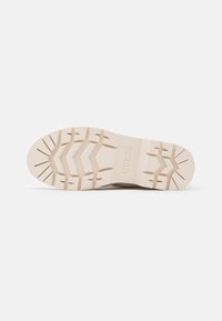 La suola delle scarpe presenta una gomma beige testurizzata con un motivo a zigzag, il logo "GUESS" impresso, una costruzione durevole e una leggera curvatura.