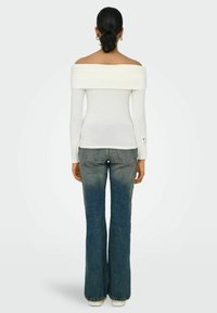 Hvid off-shoulder top med lange ærmer, parret med flagrende blå jeans. Toppen har en foldet halsudskæring og en tætsiddende silhuet.