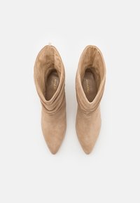 Bottines en daim beige avec un design ample, un bout pointu et une texture lisse. Dotées d'une boucle pour un enfilage facile.