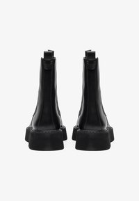 Bottines en cuir noir à semelle épaisse, avec un bout arrondi et des languettes à l'arrière. Texture lisse avec des détails de couture minimes.