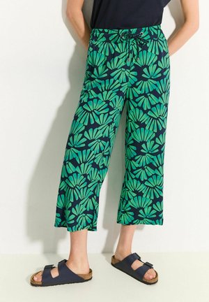 Pantaloni con stampa a foglie verdi, con vita elastica e coulisse. Tessuto leggero, lunghezza cropped, abbinati a sandali scuri.