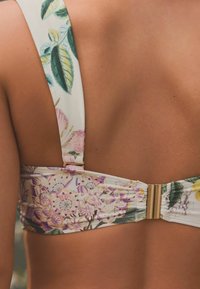 Bikini top s cvjetnim uzorkom u bijeloj boji, s raznobojnim cvjetovima i lišćem. Uključuje zlatni kopčasti detalj na stražnjoj strani.