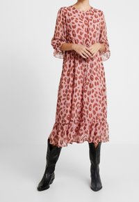 Růžová leopardí vzorovaná šaty vyrobené z lehkého chiffon, s dlouhými rukávy, volánkovým lemem a kombinované s černými kovbojskými botami.