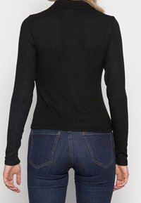 Svart ribbad långärmad topp med krage, figursydd silhuett och textilstruktur. Matchad med blå denimjeans.