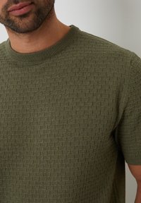 Olijfgroen gebreid sweater met een gestructureerd ruitpatroon, korte mouwen en een geribde halslijn. Zachte, lichte stof.