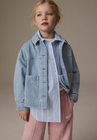 Randig blå denimjacka över en ljusblå skjorta med knappar och rosa samt vita ränder, ihop med ljusrosa sweatpants.