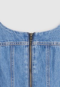 Gros plan d'un vêtement en jean bleu avec une fermeture éclair métallique centrale et des détails de couture marron visibles.