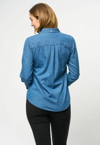 Denim shirt, medium blue, lange mouwen, knoopsluiting, puntkraag, rugplooi, afgeronde zoom. Gecombineerd met zwarte broek.