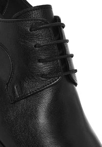 Zwarte gepolijste leren nette schoen met gesloten vetsluiting en een gladde, afgeronde neus, getoond in een close-up.