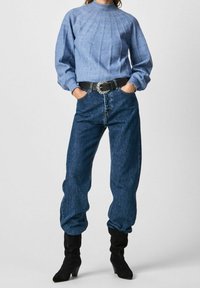 Niebieski sweter z dzianiny o prążkowanym wzorze, z wysokim dekoltem, w połączeniu ze luźnymi dżinsami. Czarny pasek ze srebrną klamrą i czarne kozaki za kolano.