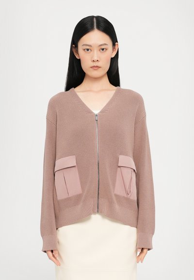 Ritsjack in licht mauve, met textuur gebreide stof. Beschikt over twee voorzakken met kleppen en ribgebreide boorden en zoom. V-hals ontwerp.