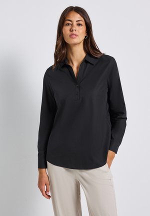 Zwarte langling-shirt met een kraag, voorzien van een gedeeltelijke knoopsluiting en een gladde stoftextuur. Gemaakt in combinatie met lichtgekleurde broeken.