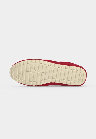 Semelle de chaussure avec une bande de roulement en caoutchouc beige comportant des motifs rectangulaires, fixée à une tige de chaussure rouge sur fond blanc.