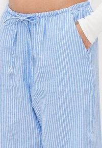 Calças leves listradas em azul e branco com cintura elástica, detalhe de cordão e bolsos laterais. O tecido tem uma textura suave.