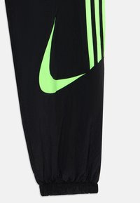 Svarta träningsbyxor med neongrön Nike-logotyp, med textilstruktur, elastiska muddar och tre vertikala svarta ränder på sidan.