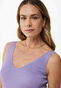 Fioletowy, prążkowany top na ramiączkach z głębokim dekoltem w kształcie litery V, dopasowany krój i cienkie ramiączka. Złoty, zakrzywiony naszyjnik podkreśla dekolt.