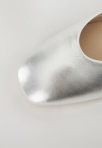 Chaussure à enfiler en cuir argenté avec un bout carré arrondi et une texture lisse, dotée d'une doublure intérieure beige.