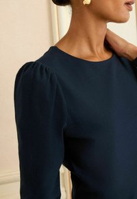 Laivaston sininen blusa, jossa on puffattuja hihoja ja pyöreä pääntie, valmistettu sileästä kankaasta, tiiviissä siluetissa ja hienovaraisessa tekstuurissa.