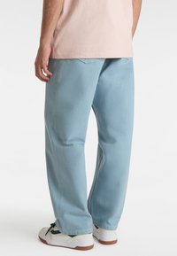 Light blue, loose-fitting pants, made from textured fabric, with back pockets, paired with white sneakers featuring green accents.