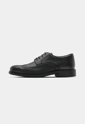 Black leather oxford shoe with brogue detailing, round toe, and laces. Flat rubber sole with a slight heel. Smooth texture, classic design.