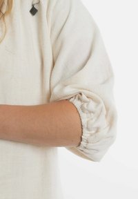 Crème-kleurige linnen top met opgeblazen mouwen en elastische manchetten, die een zachte, gestructureerde stof laat zien en een klein decoratief label heeft.