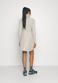 Jupe-culotte beige clair avec une texture lisse et résistante à l'eau, dotée d'une taille élastique et de poches latérales, associée à des chaussures de sport noires et des chaussettes rayées.