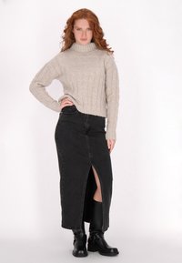 Beżowy sweter dzianinowy z wysokim kołnierzem, w zestawieniu z czarną spódnicą dżinsową z rozcięciem z przodu. Modelka nosi czarne kozaki za kolano.