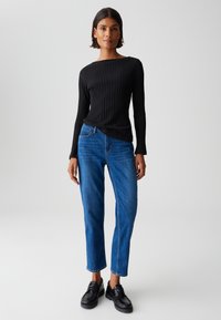 Schwarzes, geripptes Langarmoberteil kombiniert mit blauen, schmalen Jeans und schwarzen Schnürschuhen. Einfaches Design, figurbetonte Passform, strukturierter Stoff.