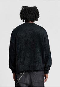 Schwarzer, flusiger Pullover mit langen Ärmeln, rundem Hals und lockerer Passform. Auffällige Textur, die weich und fluffig erscheint. Kombiniert mit dunklen Jeans.