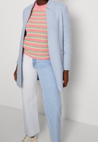 Světle modrý blazer se strukturovaným designem, nošený přes pletený svetr s růžovými a zelenými pruhy. Dvojice světle modrých a bílých džínových kalhot.
