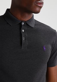 Mörkgrå polo skjorta i strukturerad bomull med en knapplist med tre knappar och en liten lila logotyp på bröstet. Kortsleeves.