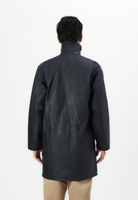 Must musta, veekindel jakk kõrge kaelusega, pikkade varrukatega ja sirge lõikega, millel on sile tekstuur ja minimalistlik disain.