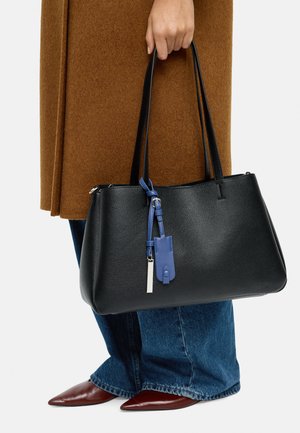 Czarna skórzana torba na ramię z dwoma długimi uchwytami, z niebieskim skórzanym breloczkiem i srebrną metką, gładka faktura, wyraźnie zdefiniowany kształt.