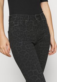Jeans de mezclilla con estampado de leopardo negro y corte slim, que cuentan con cierre de botón y cremallera, bolsillos frontales y una superficie texturizada sutil.