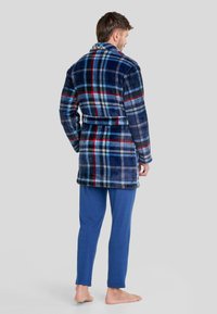 Bata de baño de forro polar en cuadros de color marino, rojo y azul claro, con amplio cuello y cinturón, combinada con pantalones azul sólidos. Textura suave y corte casual.