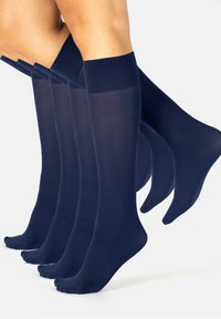 Cuatro pares de piernas que llevan calcetas azul marino hasta la rodilla en medio de un paso sobre un fondo blanco.